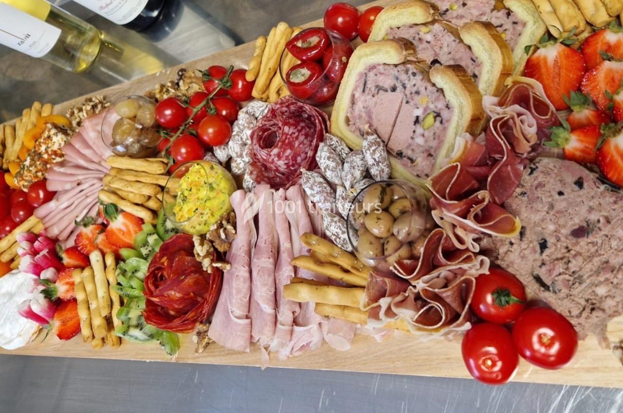 Plateau de charcuterie et fromages avec pains, fruits frais, légumes, noix et condiments, présenté sur une planche en bois.