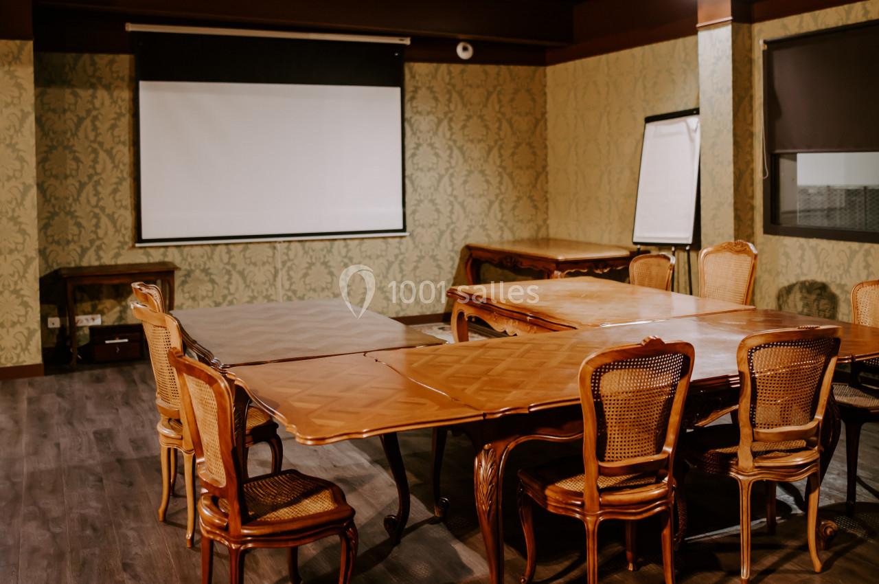 Salle de réunion avec tables en bois, chaises en osier, écran de projection et tableau blanc sur un mur décoré.