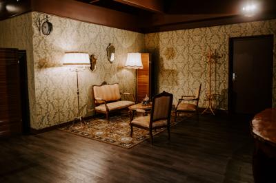 Salon vintage avec canapé, fauteuils, table basse en bois, tapis oriental, lampes et miroirs sur un mur à motifs.