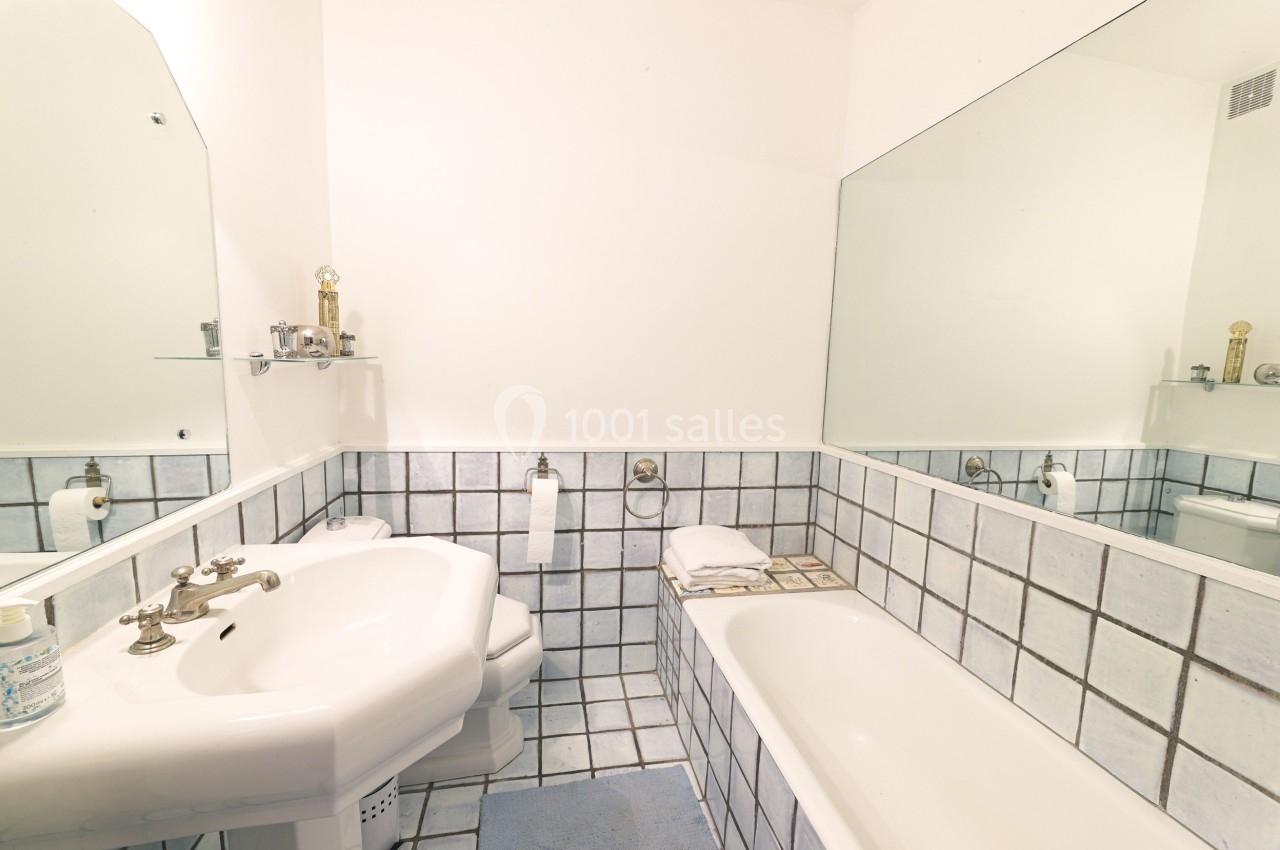 Salle de bain avec carrelage blanc et bleu, lavabo, baignoire, miroir mural et étagère avec accessoires.
