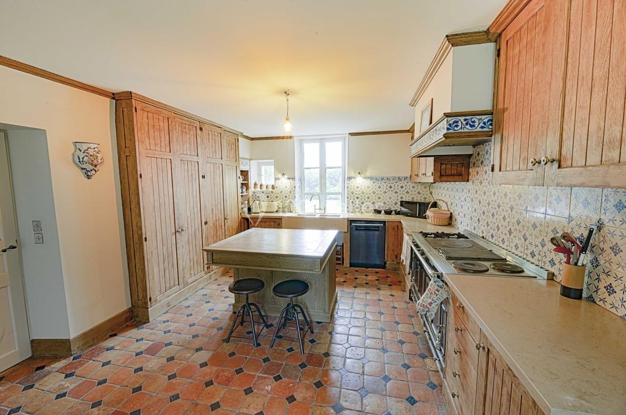 Cuisine lumineuse avec meubles en bois, îlot central, carrelage en terre cuite et crédence à motifs.