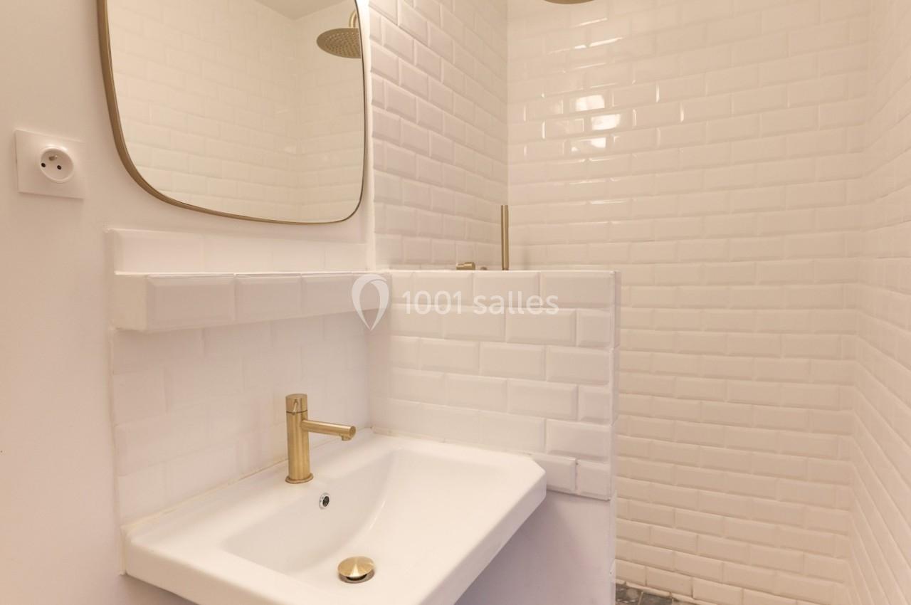 Lavabo blanc avec robinet doré, miroir rectangulaire et mur en carrelage blanc dans une salle de bain.