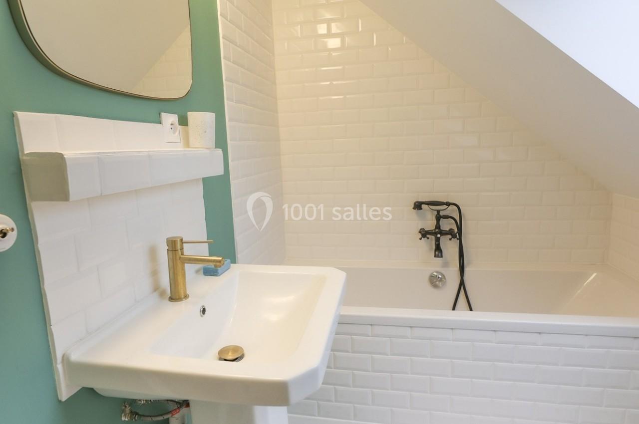 Salle de bain avec lavabo blanc, robinet doré, baignoire blanche et mur carrelé en sous-pente.