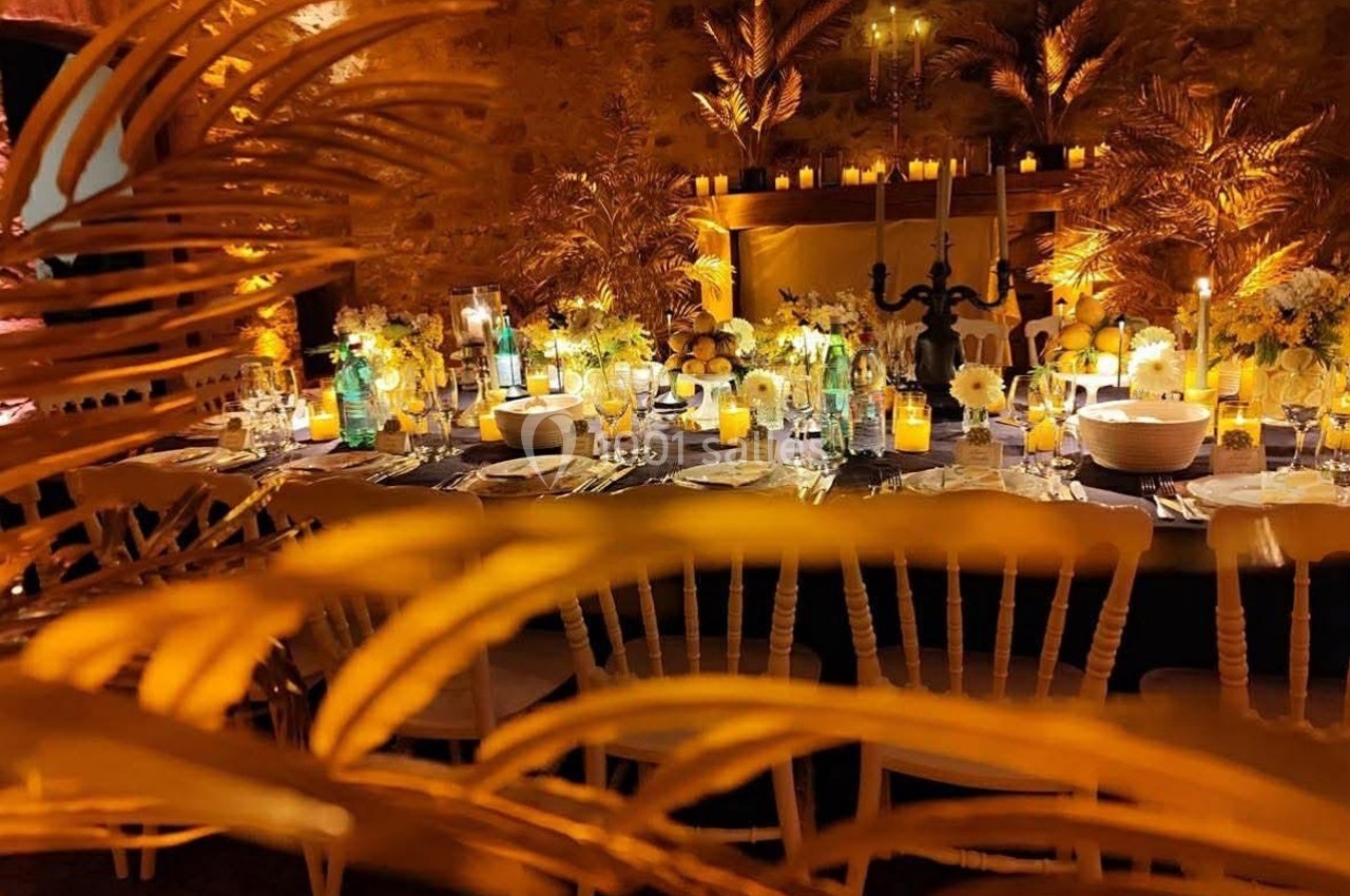 Table décorée pour un dîner élégant, entourée de bougies, fleurs et palmiers dorés dans une ambiance chaleureuse.