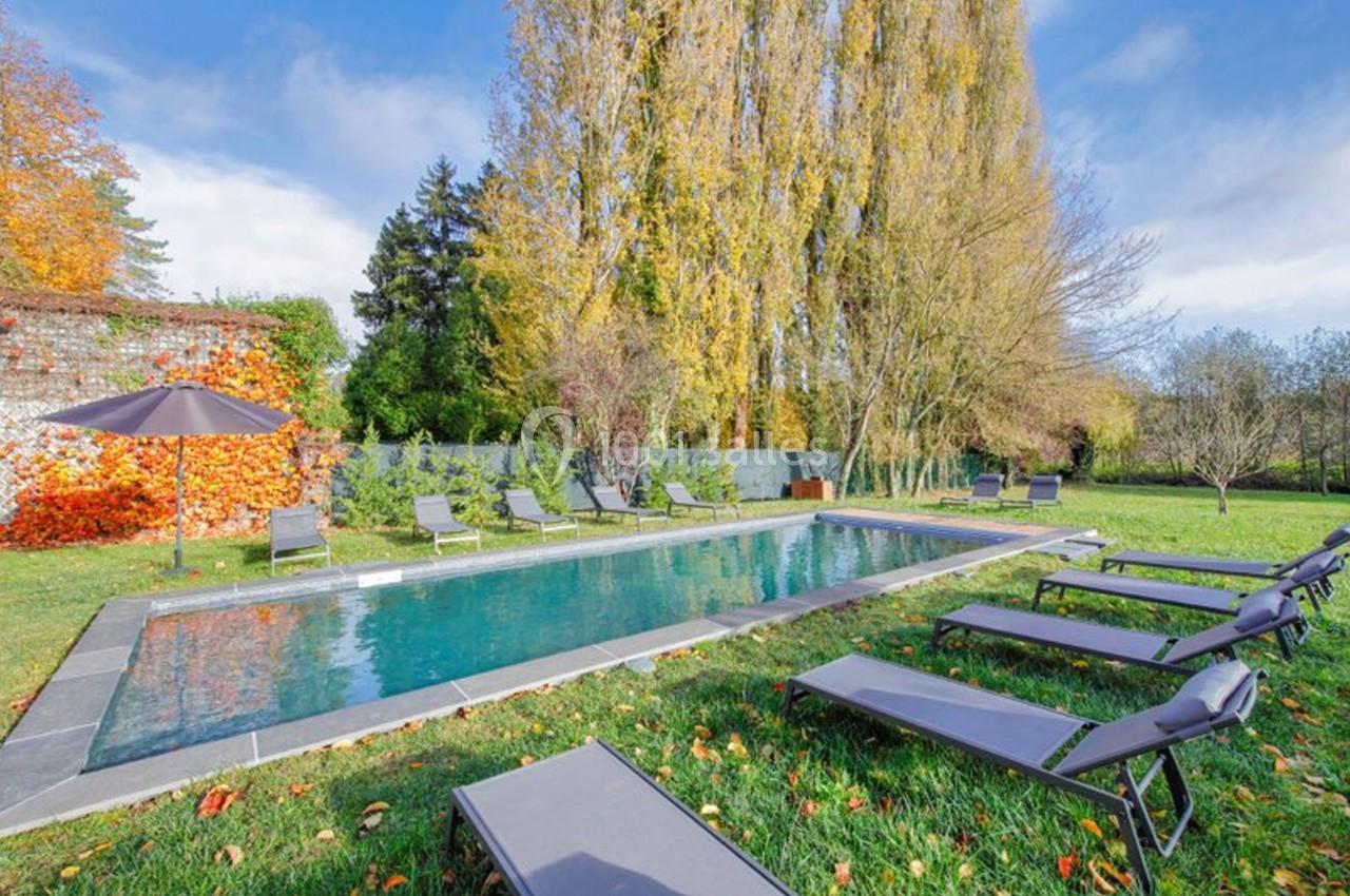 Piscine extérieure entourée de chaises longues, arbres aux feuilles d'automne et pelouse verte.