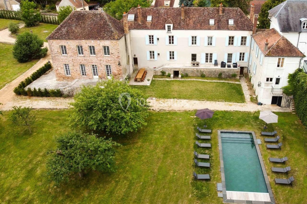 Vue aérienne d'une grande maison ancienne avec jardin, piscine rectangulaire et chaises longues disposées autour.