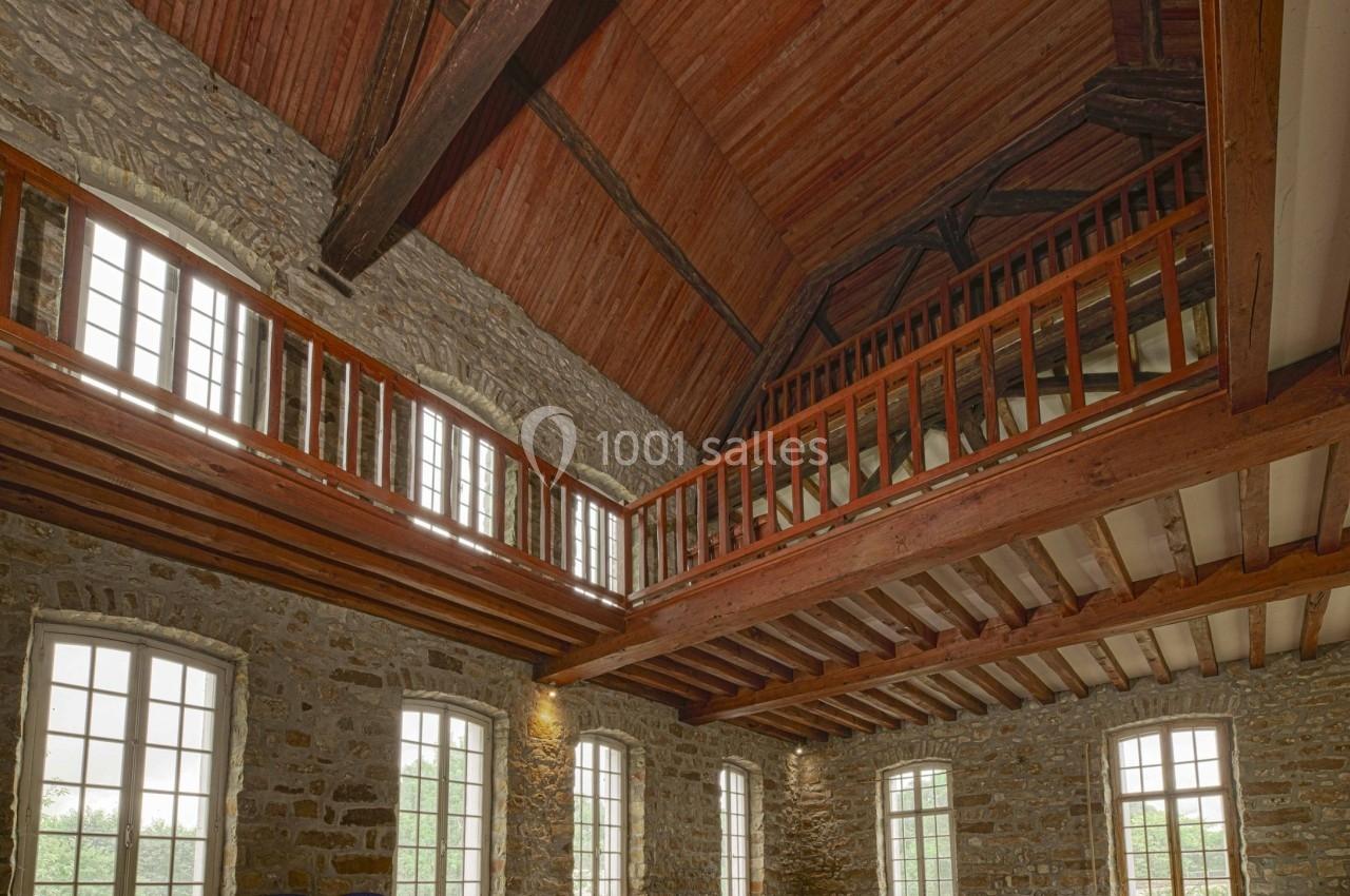 Salle spacieuse avec murs en pierre, charpente en bois apparente, grandes fenêtres et tables de ping-pong pliées.