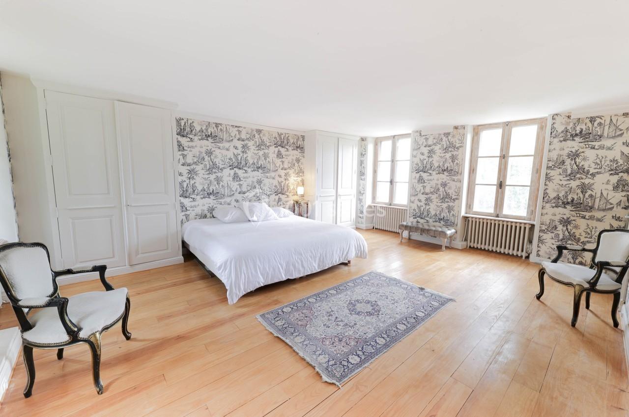 Chambre lumineuse avec lit double, murs ornés de papier peint à motifs, parquet en bois clair et tapis au sol.