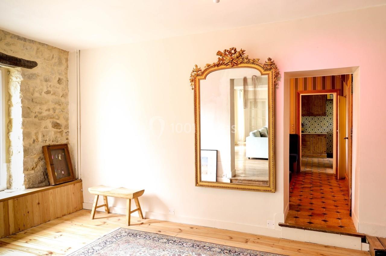 Miroir doré accroché à un mur clair, reflétant une pièce lumineuse avec un canapé, dans un intérieur rustique.