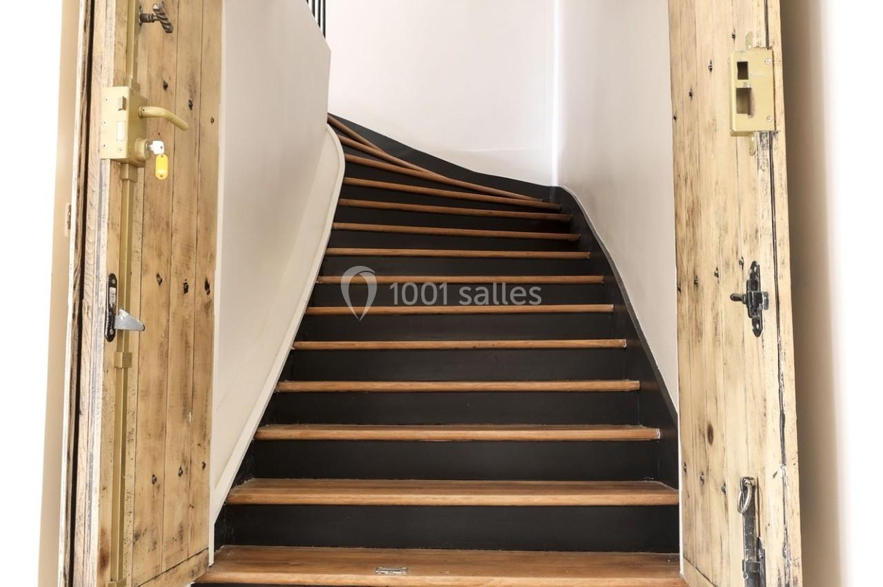 Escalier en bois avec des contremarches noires, encadré par une porte en bois ancien légèrement ouverte.