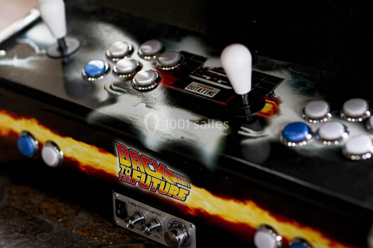 Borne d'arcade rétro avec deux joysticks, boutons colorés et décorations inspirées de ’Retour vers le futur’.