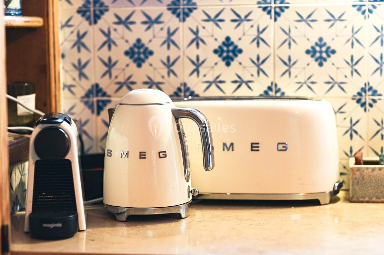 Bouilloire, grille-pain et machine à café sur un plan de travail devant un carrelage à motifs bleus.