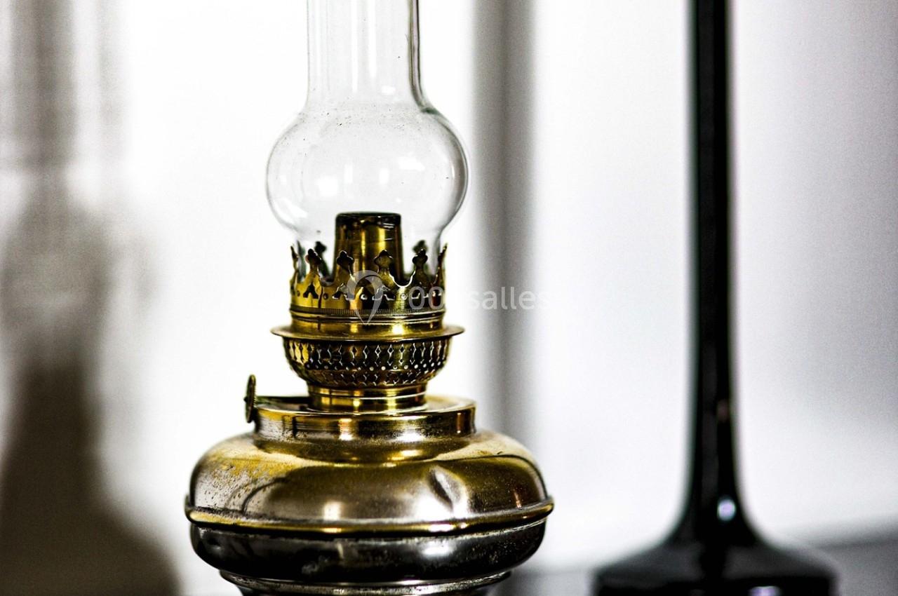 Lampe à huile en métal doré avec un verre transparent, posée sur une surface sombre.