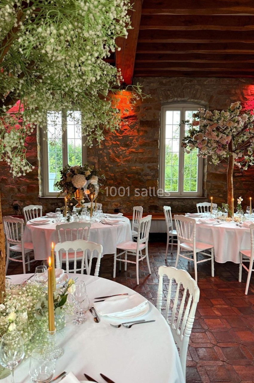 Salle de réception décorée avec des tables rondes, nappes blanches, chandeliers dorés et arrangements floraux élégants.