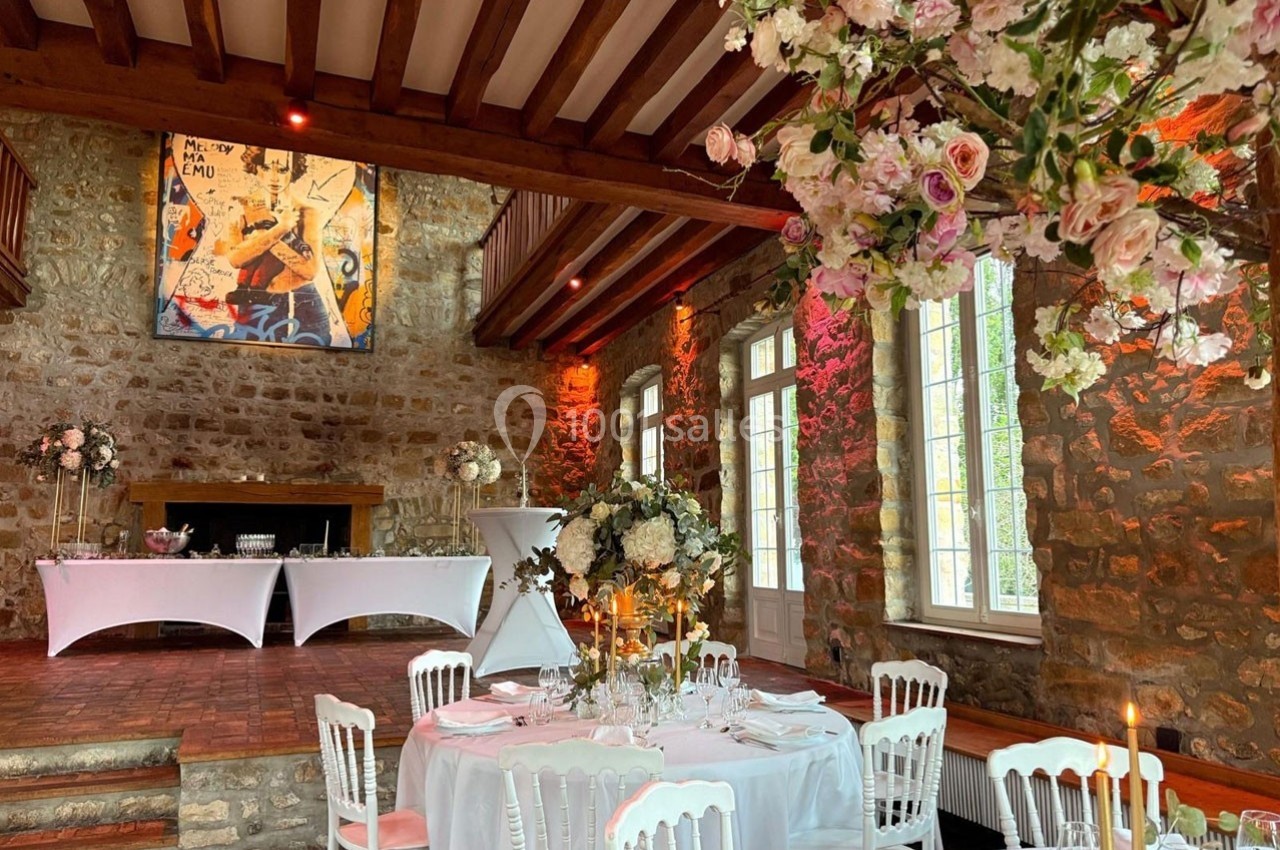Salle de réception en pierre avec tables décorées de fleurs, chandeliers et éclairage chaleureux.