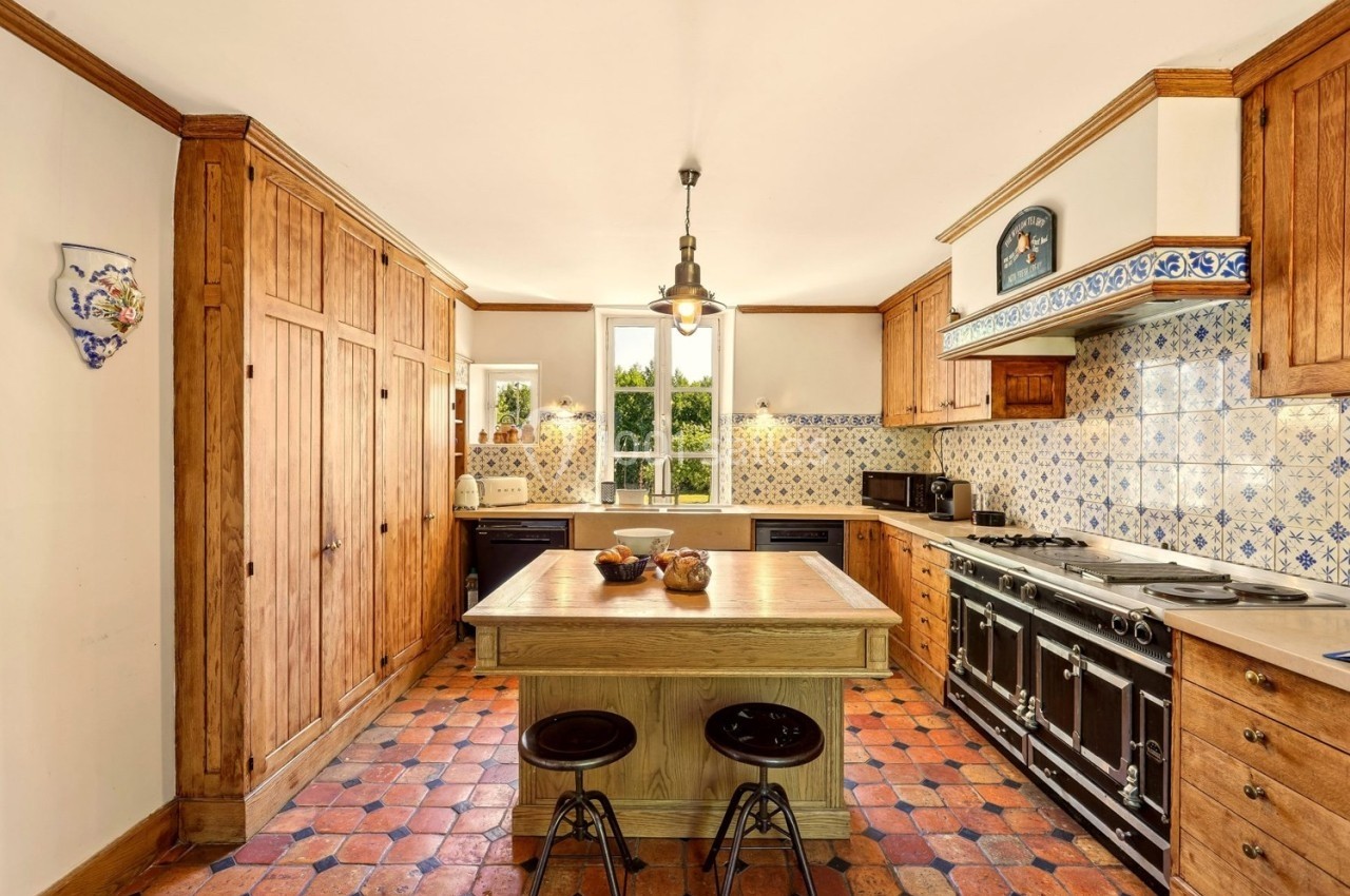 Cuisine traditionnelle avec meubles en bois, carrelage au sol, îlot central et grande cuisinière noire.