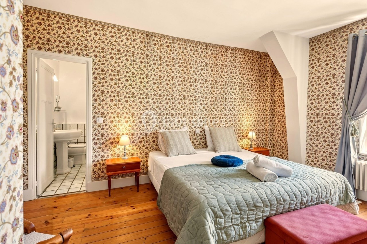 Chambre avec lit double, couvre-lit vert, tables de chevet, lampes allumées, papier peint fleuri et salle de bain attenante.