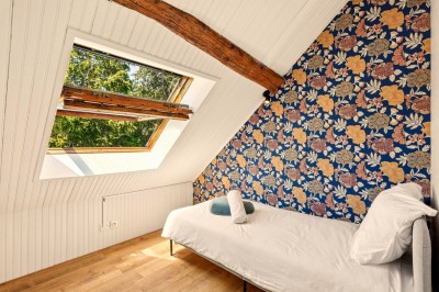 Miniature Location salle Villecerf (Seine-et-Marne) - Maison Nelson #36 Chambre lumineuse avec lit double, parquet en bois, commode, fenêtres et puits de lumière donnant sur un extérieur verdoyant.