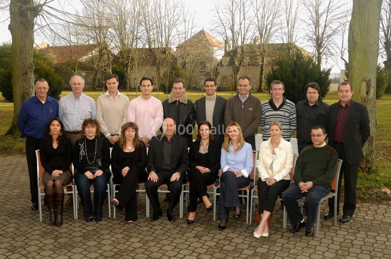 Un groupe de personnes posant en extérieur, assis et debout, sur une allée pavée devant des arbres et des bâtiments.
