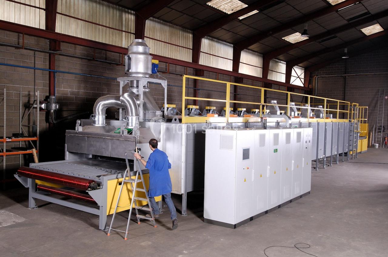 Un technicien inspecte une grande machine industrielle dans un atelier spacieux avec des équipements métalliques.
