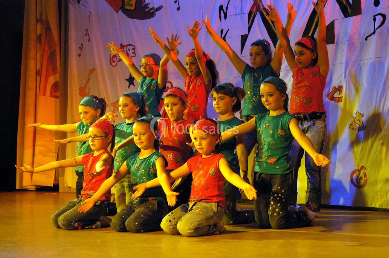 Des enfants en costume coloré exécutent une chorégraphie sur une scène décorée de motifs festifs.