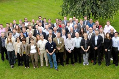 Un groupe d'adultes posant en extérieur sur une pelouse verte, avec un arbre en arrière-plan.