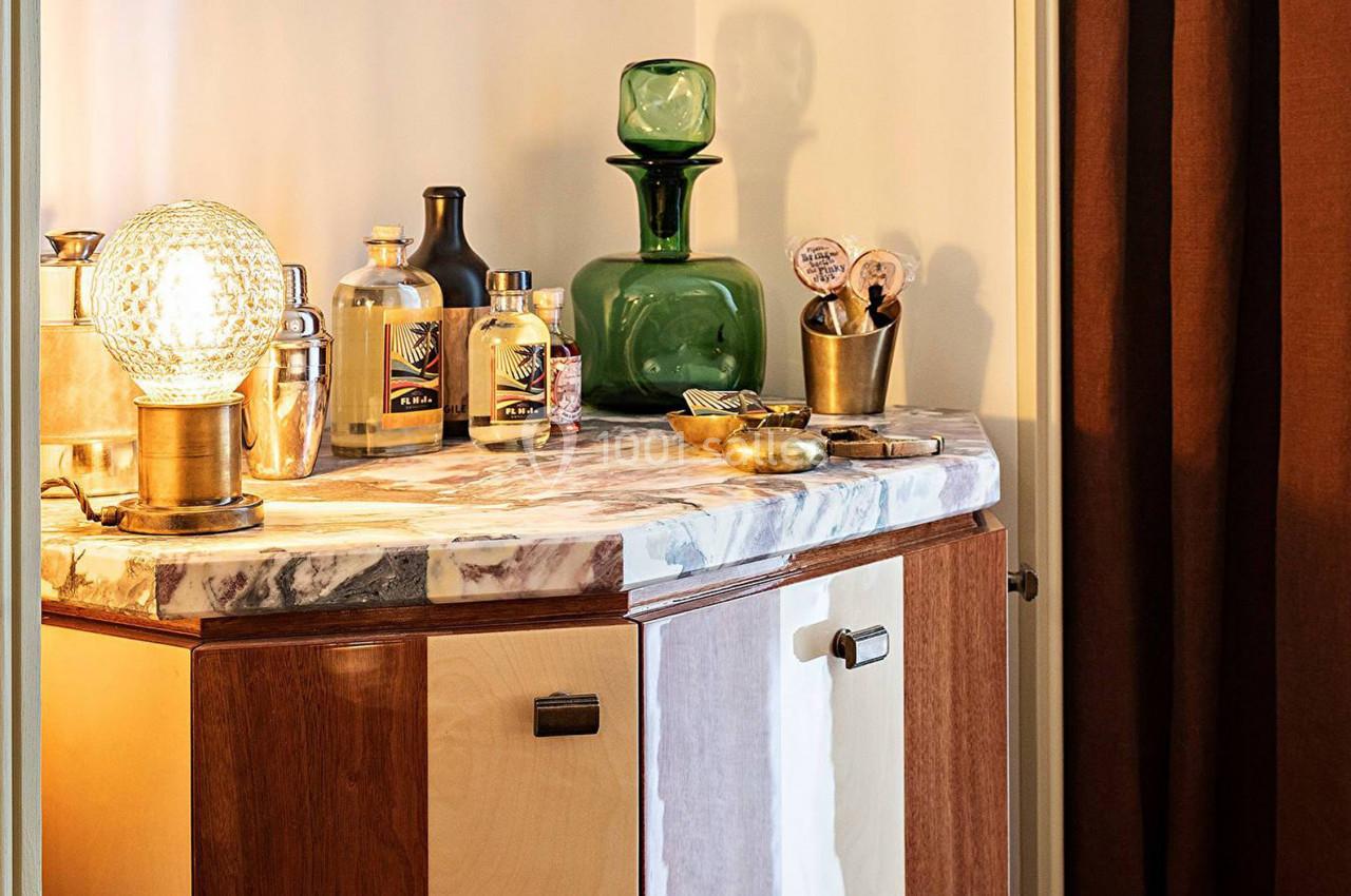 Meuble en bois avec plateau en marbre, décoré de bouteilles, objets vintage et une lampe en verre texturé.