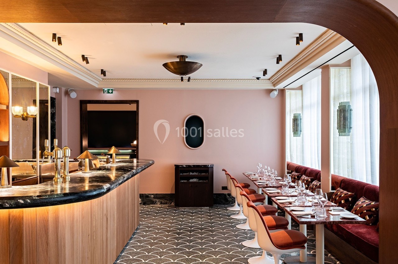 Salle de restaurant élégante avec bar en marbre, tables dressées, chaises modernes et murs aux tons pastel.
