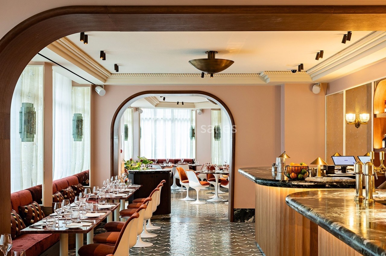 Salle de restaurant lumineuse avec tables dressées, bar en marbre et arches en bois dans un décor moderne.