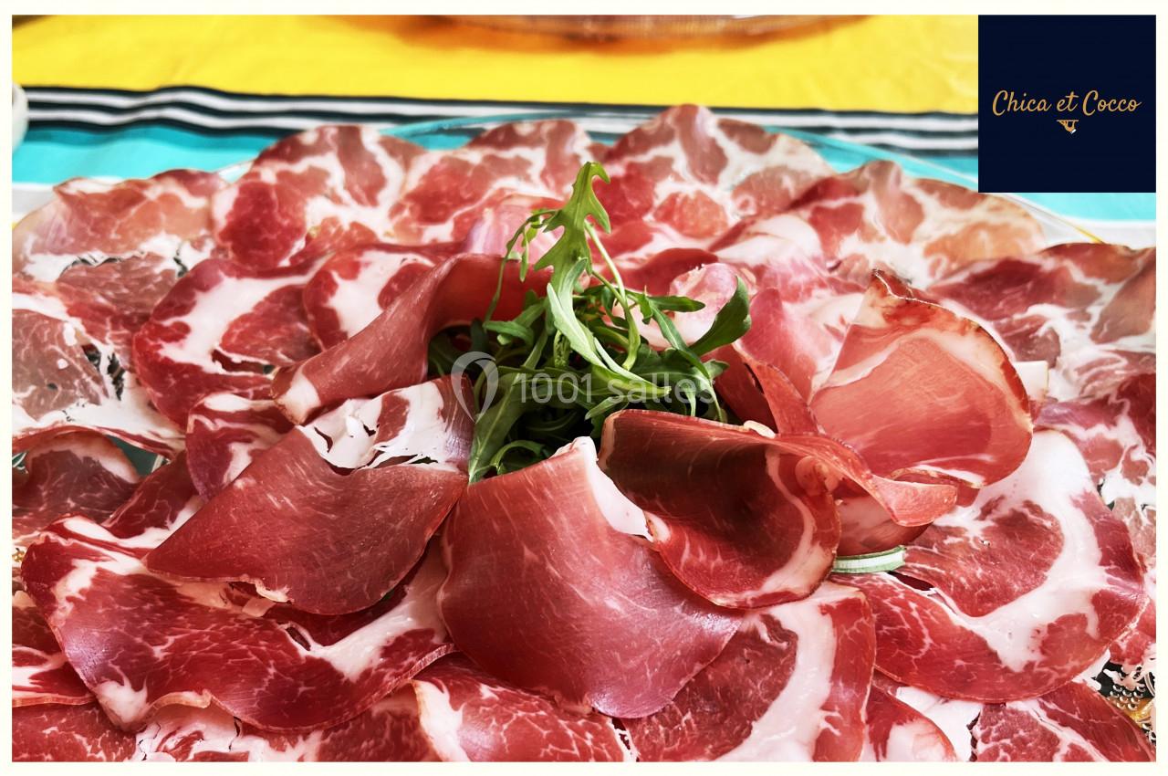 Assiette de charcuterie composée de fines tranches de viande séchée, garnie de roquette au centre.