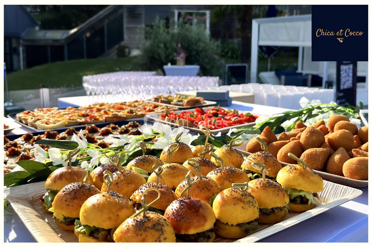 Plateau de mini-burgers, bouchées salées et verrines disposés sur une table pour un buffet en extérieur.