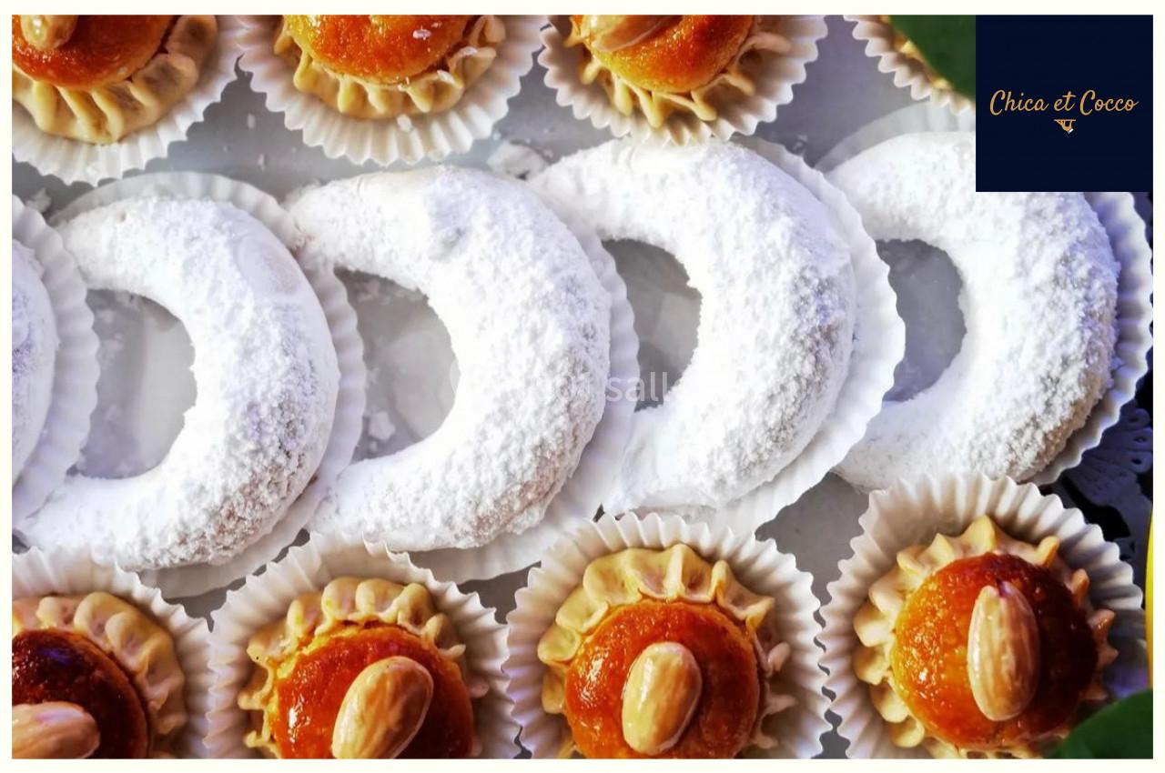 Assortiment de pâtisseries orientales, incluant des cornes de gazelle saupoudrées de sucre glace et des gâteaux aux amandes.