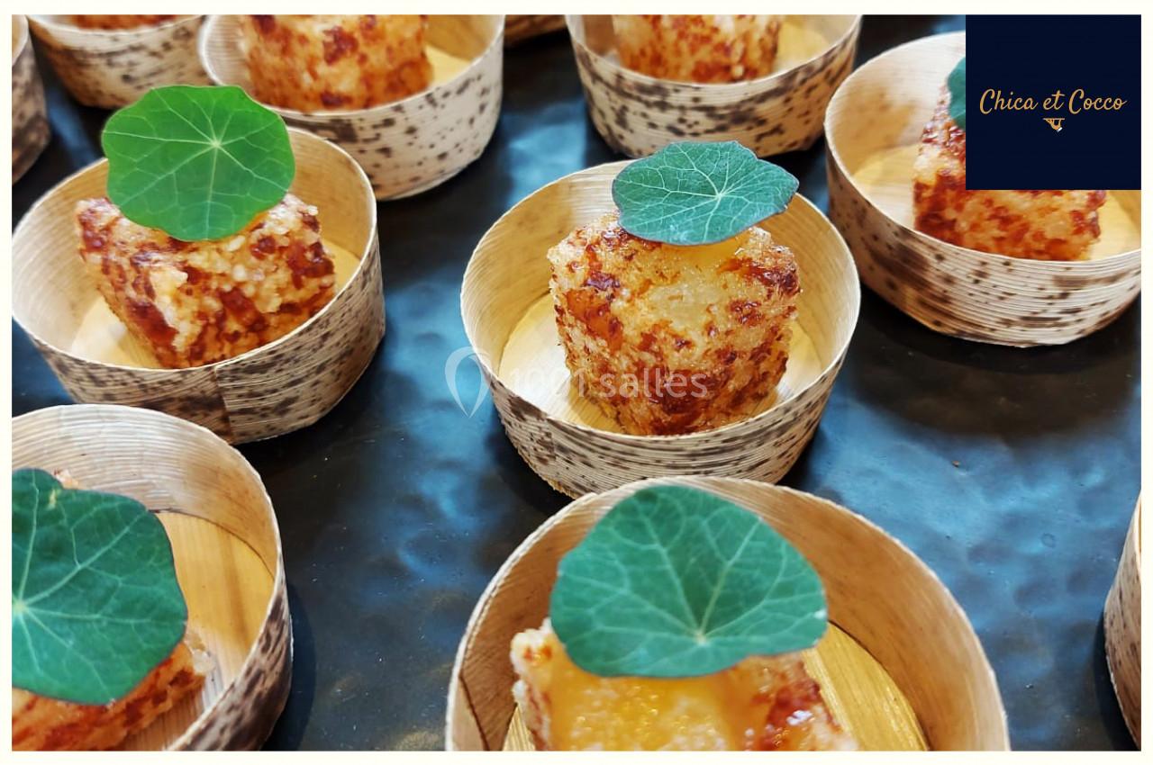 Bouchées dorées servies dans des coupelles en bambou, décorées de feuilles vertes comestibles.