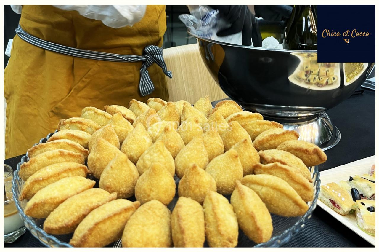 Assiette de beignets dorés disposés en cercle sur une table, avec un serveur en arrière-plan.
