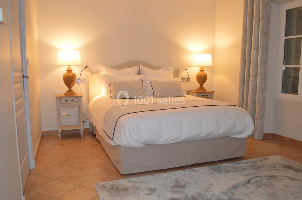 Chambre lumineuse avec un lit double, deux tables de chevet avec lampes allumées et un tapis sur un sol en carrelage.