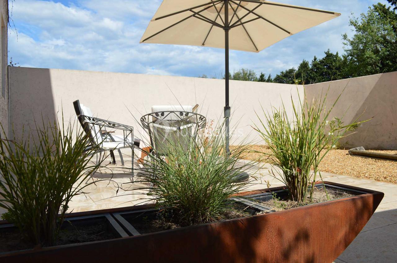 Terrasse ensoleillée avec mobilier de jardin, parasol et jardinière contenant des plantes vertes.