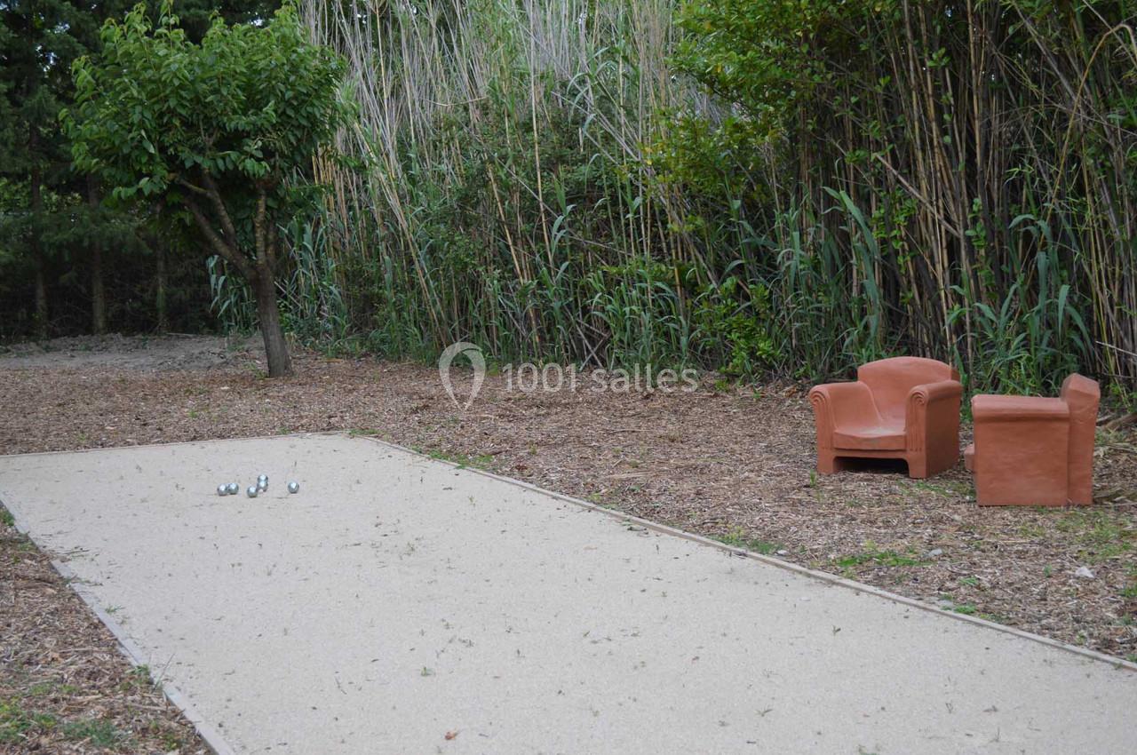 Terrain de pétanque en plein air entouré de végétation, avec deux fauteuils en terre cuite à proximité.