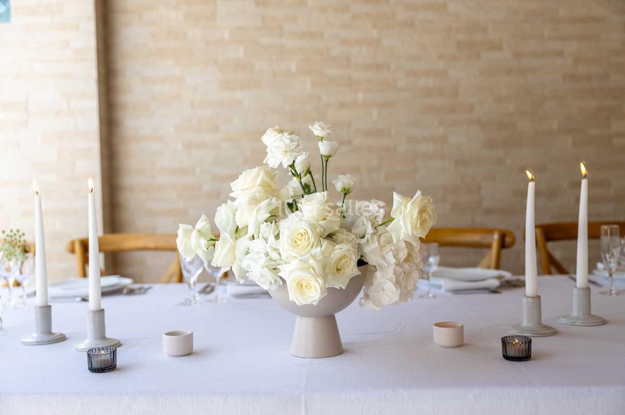 Centre de table avec un bouquet de fleurs blanches entouré de bougies allumées sur une nappe blanche.