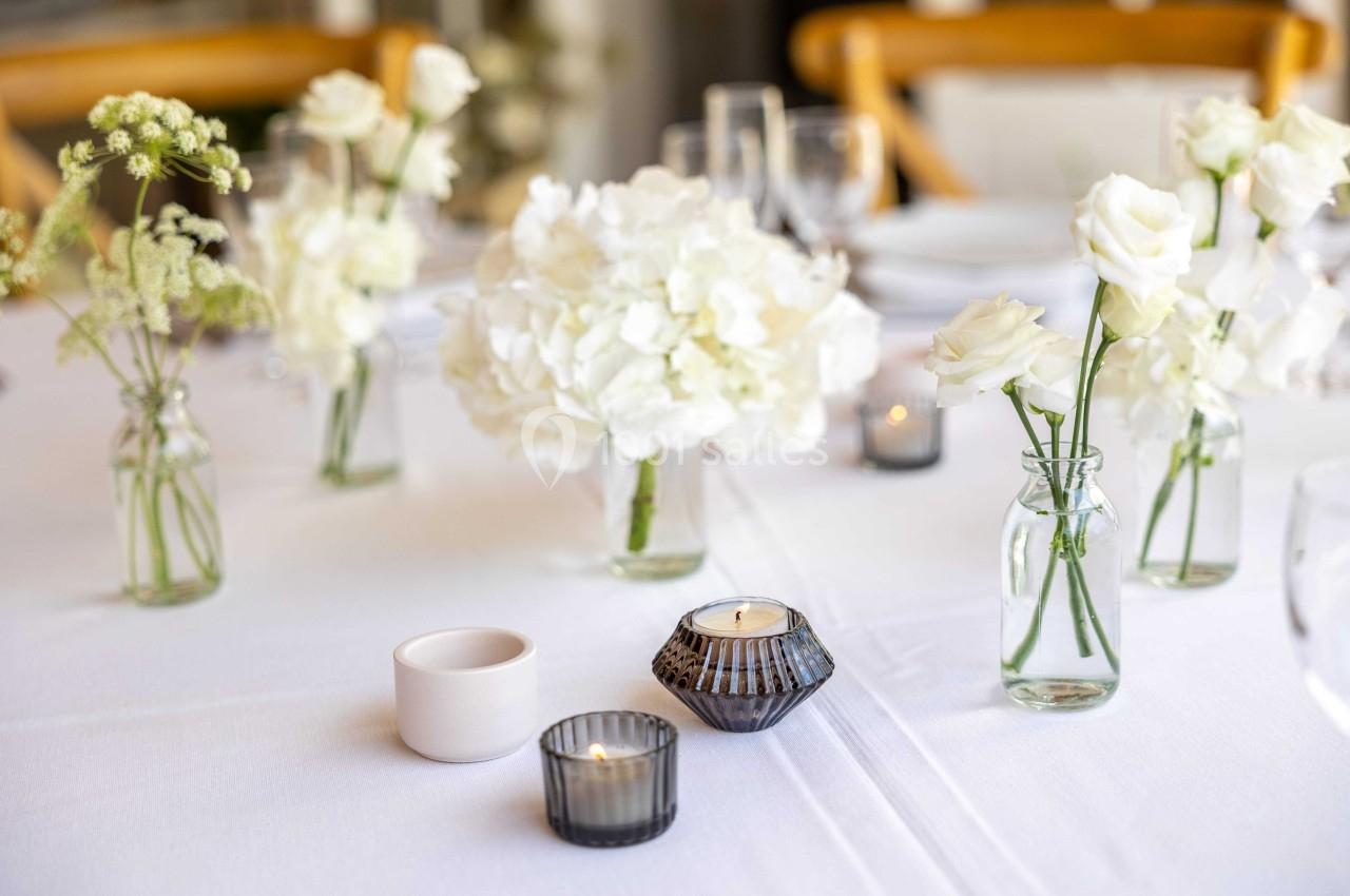 Bouquet de fleurs blanches dans des vases en verre sur une table dressée avec bougies et vaisselle élégante.