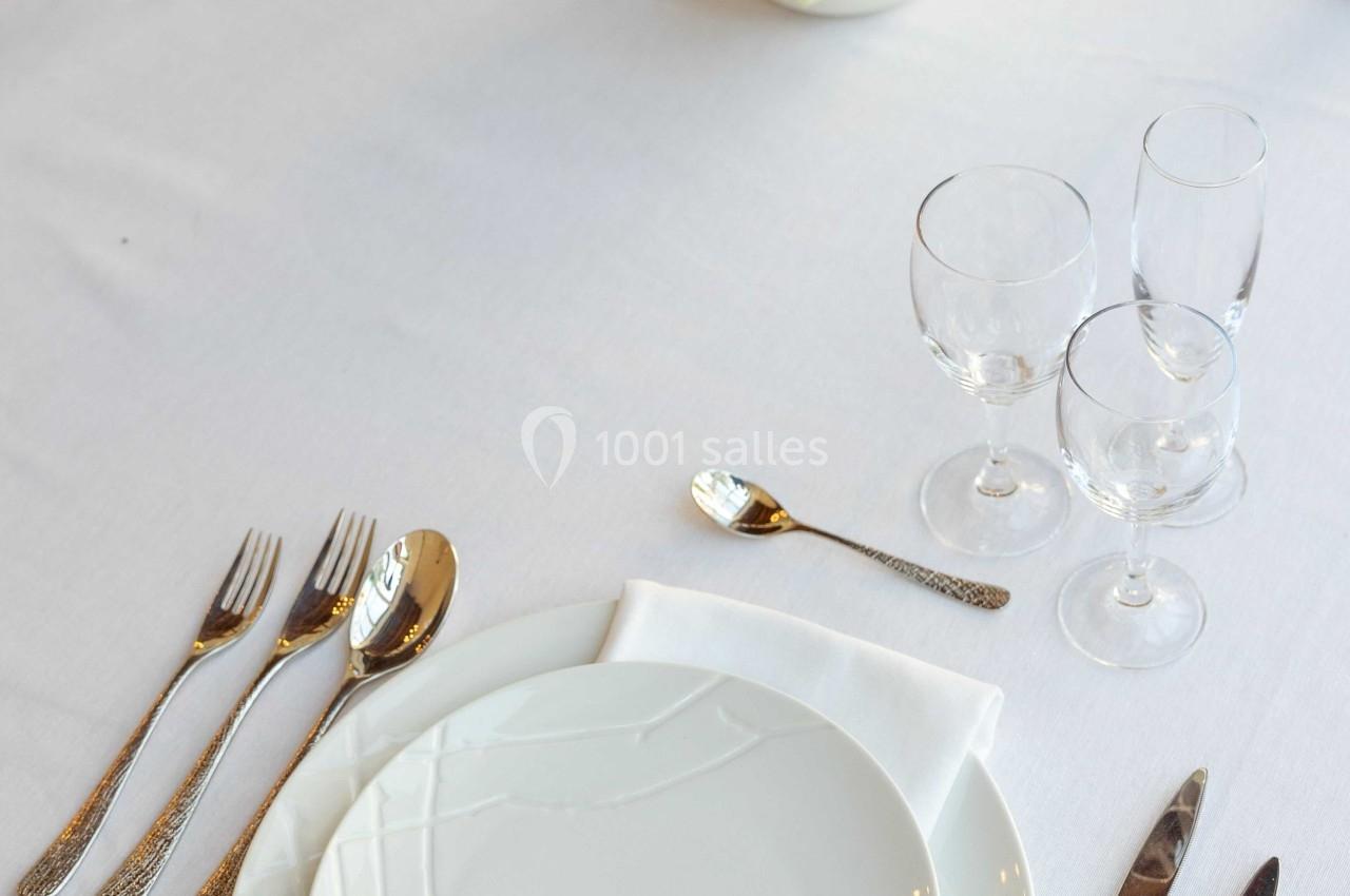 Table dressée avec assiette blanche, couverts en métal, serviette pliée, verres à pied et centre de table floral.