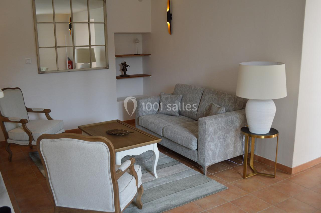 Salon lumineux avec canapé gris, fauteuils en bois clair, table basse, lampe blanche et miroir mural.