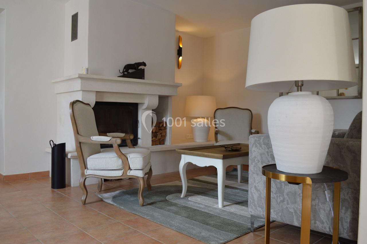 Salon lumineux avec cheminée, fauteuils en bois, table basse blanche, tapis rayé et lampes sur des tables d'appoint.