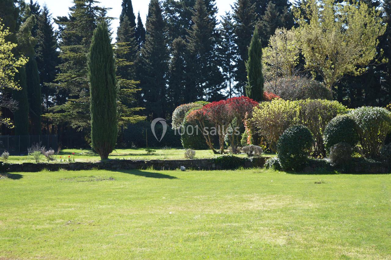 Jardin avec pelouse, arbustes taillés, arbres variés et haies colorées sous un ciel dégagé.