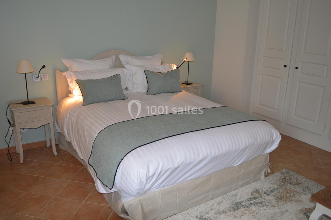 Lit double avec draps blancs et couvre-lit gris, encadré par deux tables de chevet avec lampes, dans une chambre lumineuse.