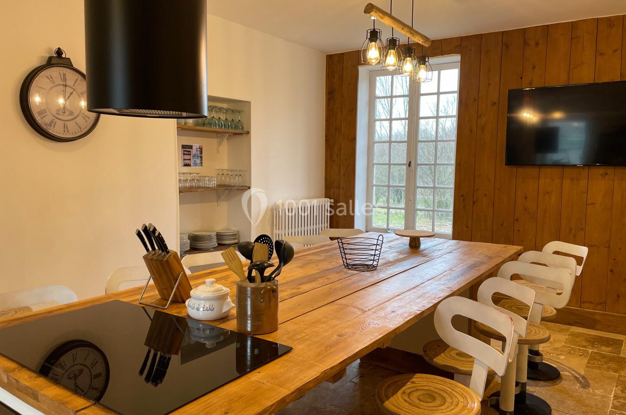 Cuisine avec une grande table en bois, chaises hautes, plaques de cuisson intégrées et éclairage suspendu.