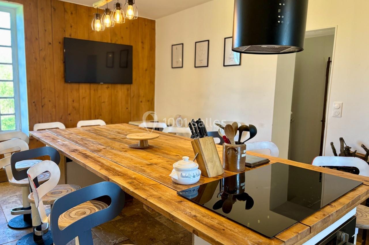 Grande table en bois entourée de chaises modernes dans une cuisine lumineuse avec plaques de cuisson et décorations murales.