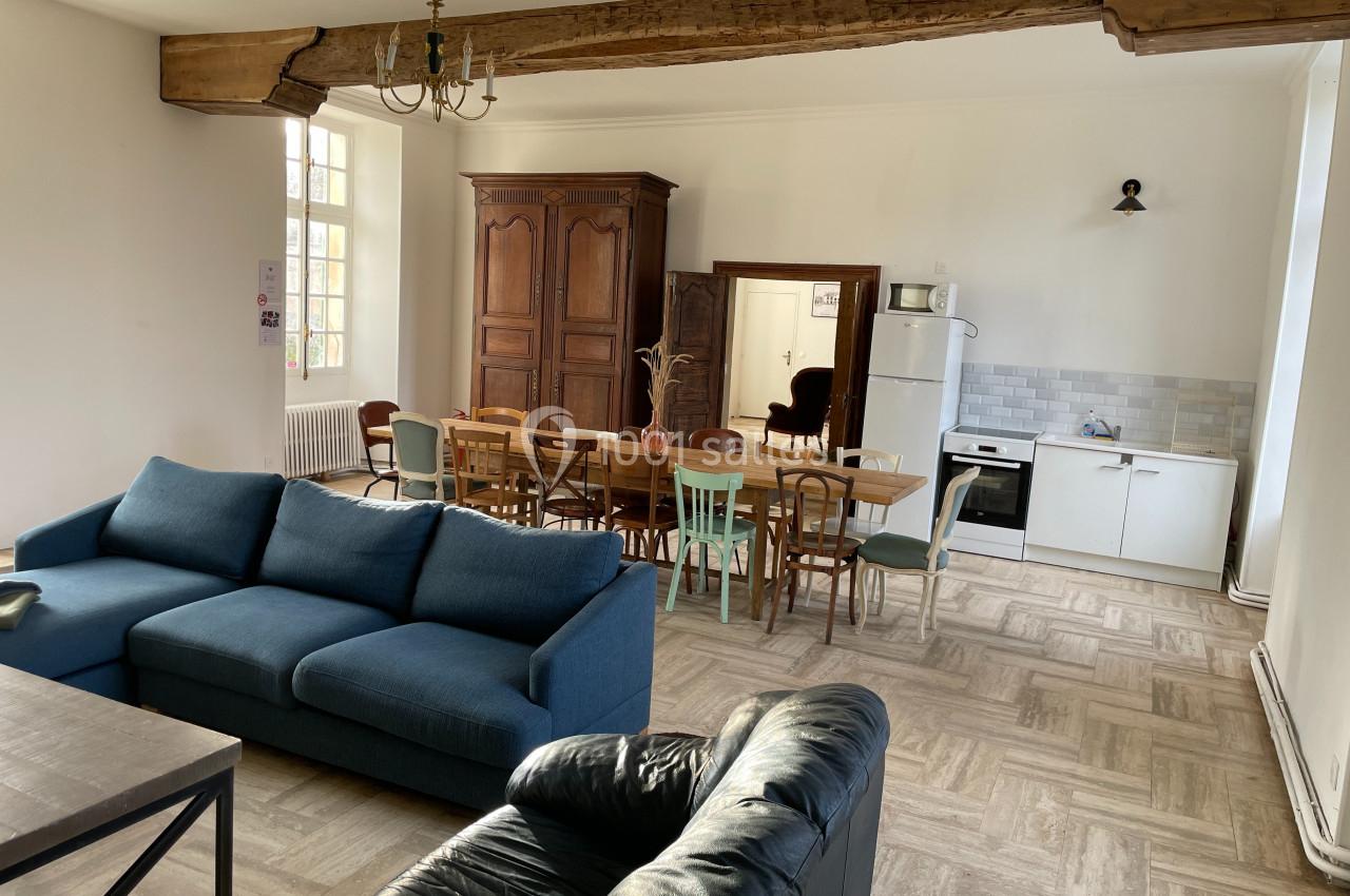 Salle de séjour lumineuse avec canapé, table à manger, armoire en bois, cuisine équipée et poutre apparente.