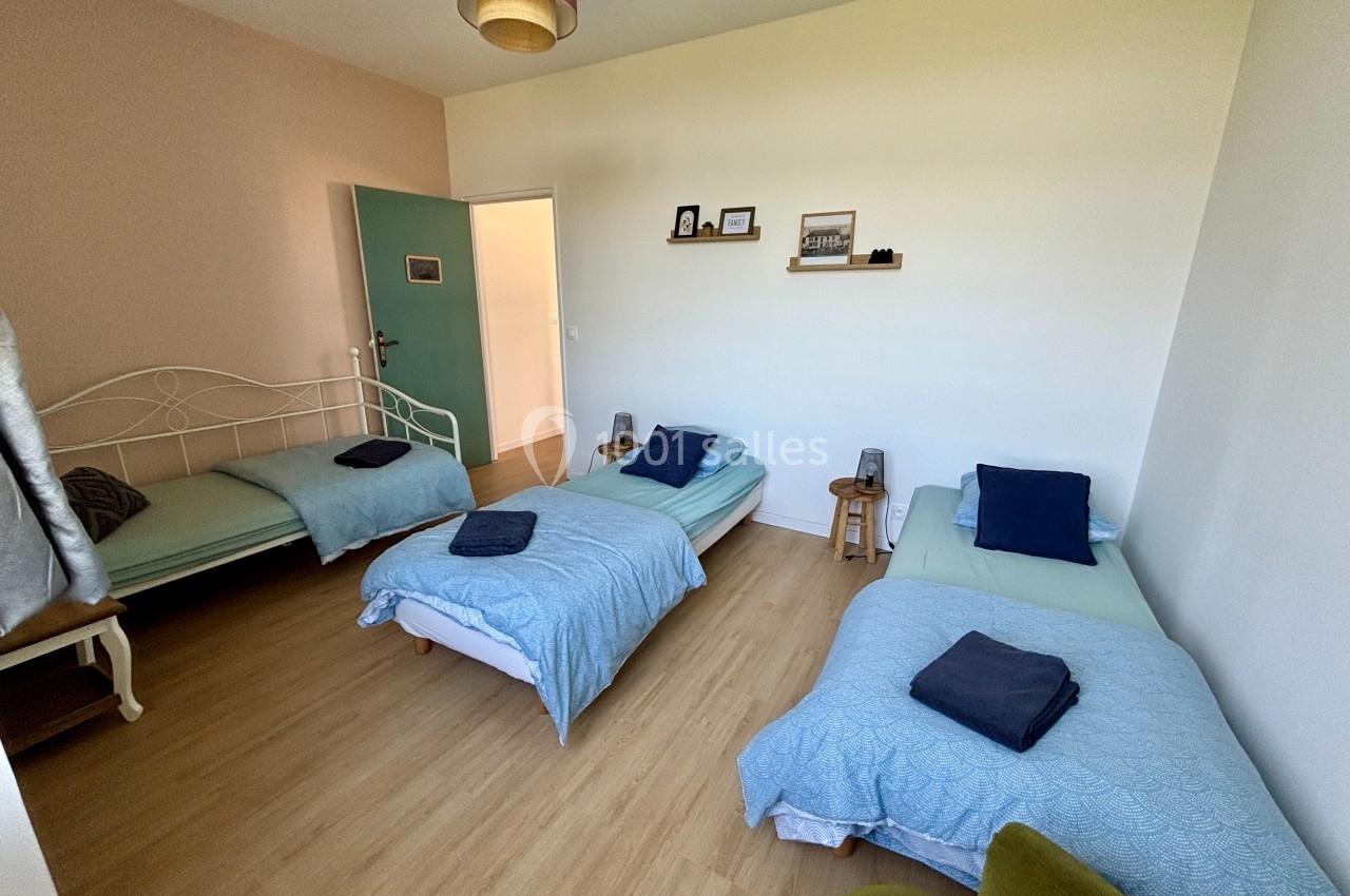 Chambre lumineuse avec trois lits simples, parquet au sol, murs clairs et décoration minimaliste.