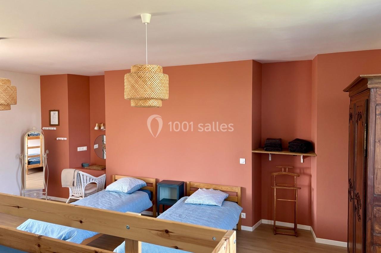 Chambre lumineuse avec murs orange, deux lits simples, mobilier en bois et éléments de décoration en rotin.