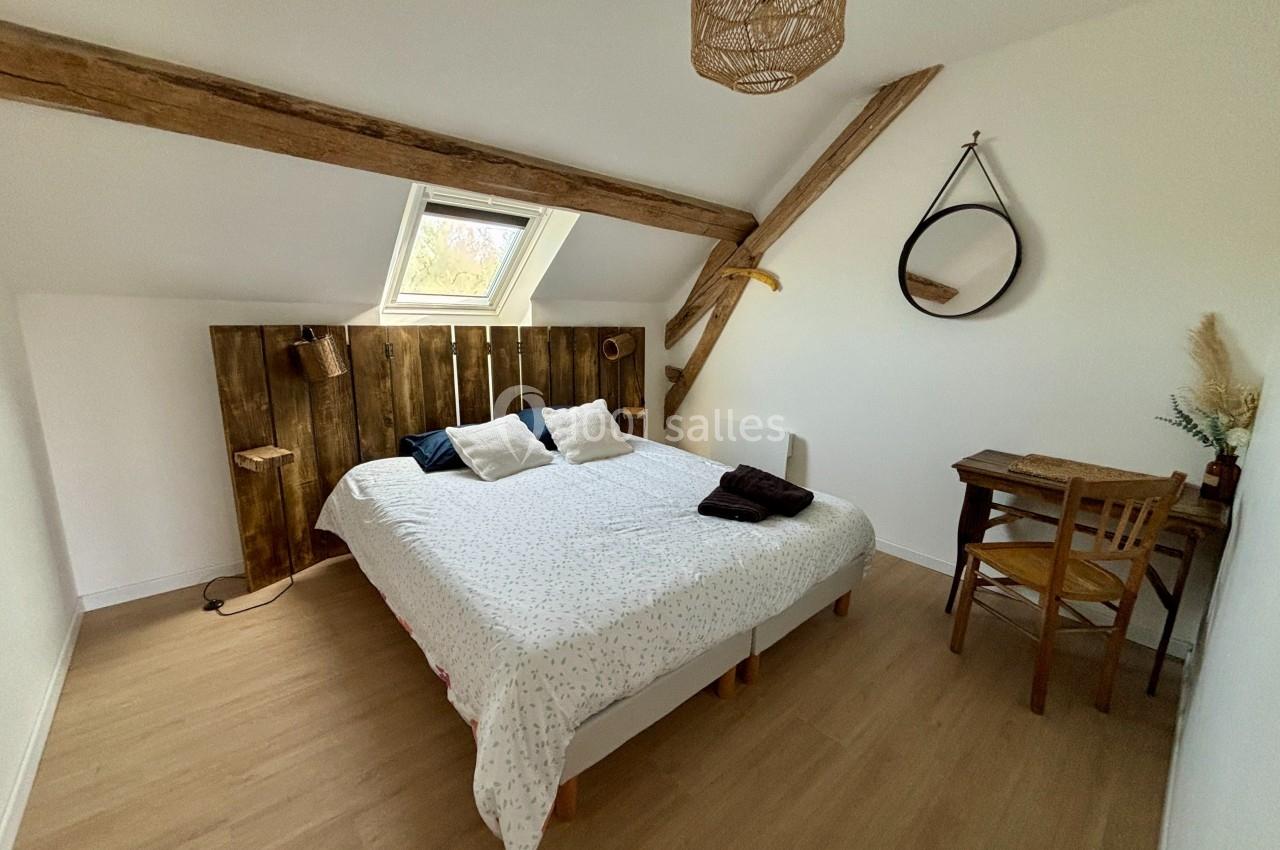 Chambre mansardée avec lit double, mobilier en bois, miroir rond et fenêtre de toit laissant entrer la lumière naturelle.